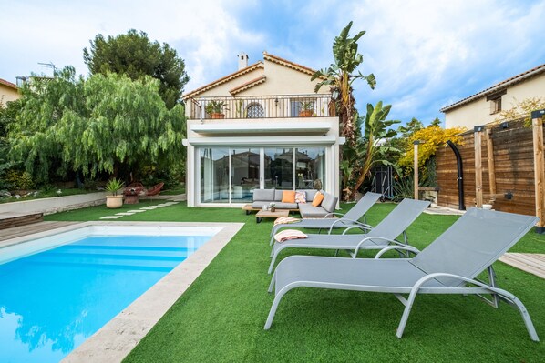 Ein modernes Haus mit Pool, einem Balkon mit Gartenmöbeln und einem gepflegten Garten.