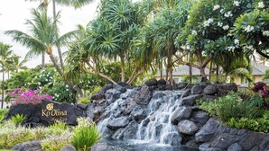 A waterfall cascading over rocks with lush greenery and a sign reading "Ko Olina Place of Joy".