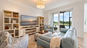A modern living room with a flat-screen TV, a grey sofa, patterned cushions, and a wooden entertainment unit. - 30-night Min. Clubhouse Open Heritage Landing Golf Club Golf Membership Transfer Included 2 Bedroom Condo (Punta Gorda)