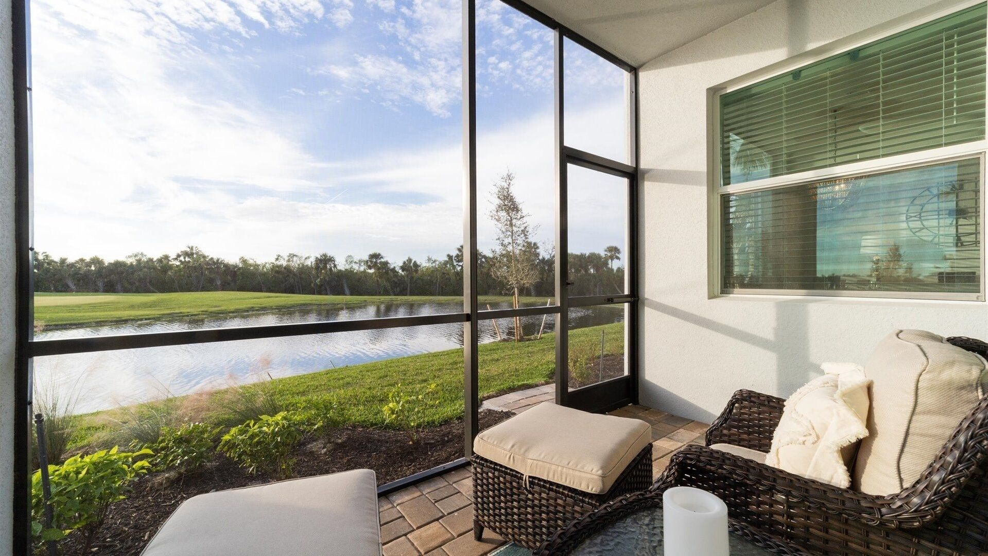 A room with large windows overlooking a lake, wicker furniture, and a view of a grassy area with trees.