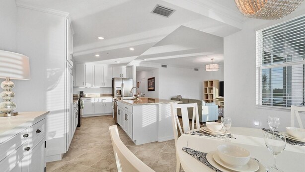 A modern kitchen with white cabinetry, a central island, and a dining area with a table set for two. - 30-night Min. Clubhouse Open Heritage Landing Golf Club Golf Membership Transfer Included 2 Bedroom Condo (Punta Gorda)