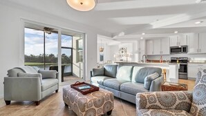 A spacious living room with a large sliding glass door leading to a balcony, a grey sofa, patterned ottoman, and a patterned armchair. - 30-night Min. Clubhouse Open Heritage Landing Golf Club Golf Membership Transfer Included 2 Bedroom Condo (Punta Gorda)