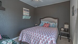 A bedroom with a bed, a nightstand, a lamp, a wall clock, a poster, and a coat rack. - Relaxing Townhome By Lemon Bay, Minutes To Beach 2 Bedroom Townhouse (Englewood)