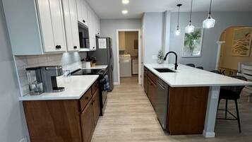 Cozinha moderna com armários brancos, uma ilha central e luminárias pendentes.