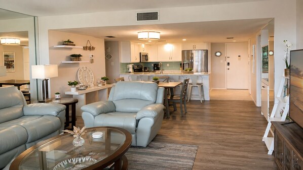 A modern living room with a sofa, a glass coffee table, and a dining area with chairs. - Anchorage Resort 2 Bedroom Condo 6th Flr, Beach Access, Pool 2 Condo (Siesta Key)