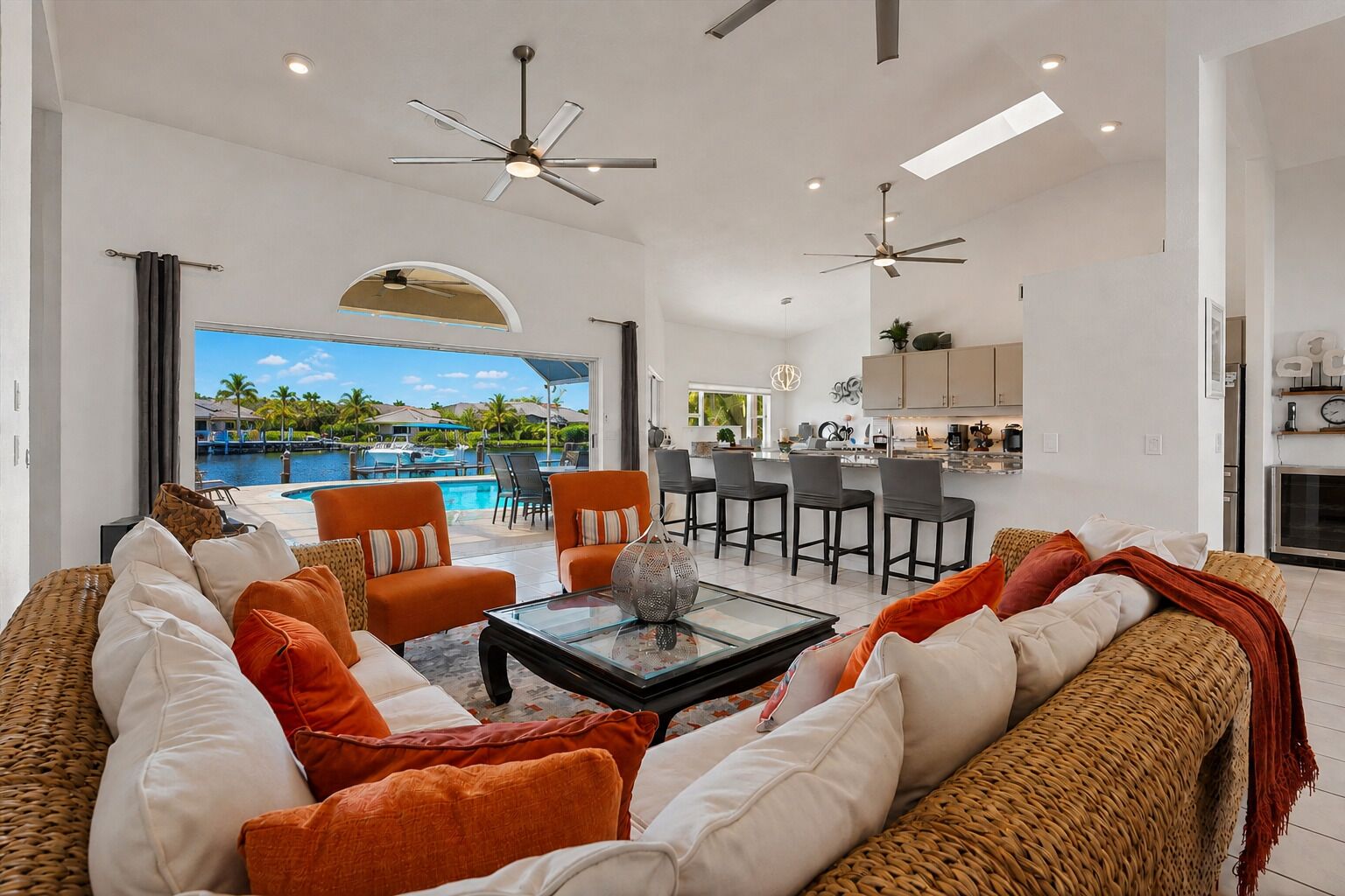 A modern living room with a pool view, two ceiling fans, and a kitchen area.