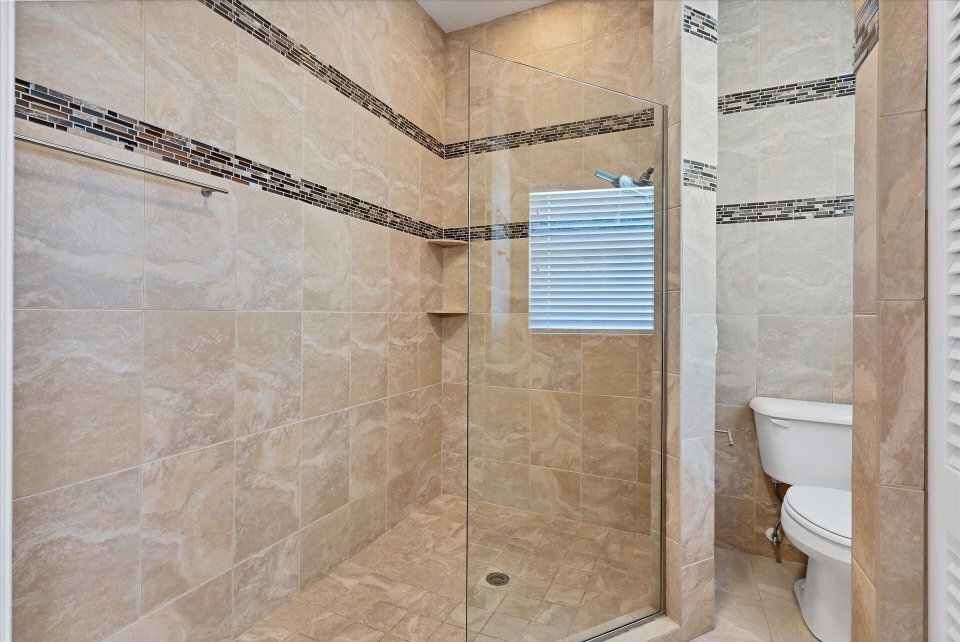 Une salle de bain avec une douche à parois de verre, des carreaux de couleur beige et des toilettes.