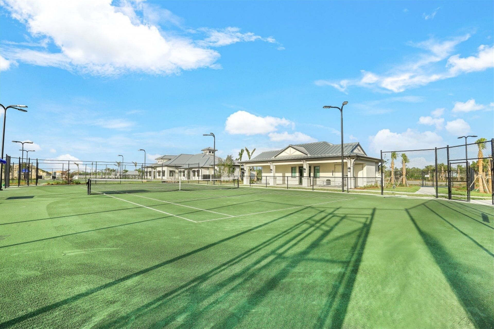 Un court de tennis avec un filet, entouré d’une clôture, et un bâtiment avec un toit visible au fond.