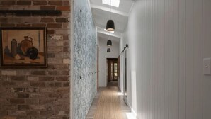 Un couloir aux murs en briques apparentes, doté d’un plancher en bois et orné d’une œuvre d’art encadrée sur le côté gauche.