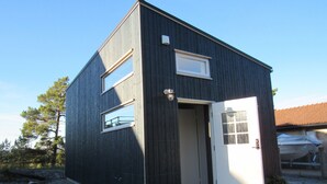 Un bâtiment de taille modeste, de couleur sombre, avec une porte blanche et deux fenêtres.