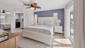 Quarto com cama, mesas de cabeceira, ventilador de teto e vista para o exterior.
