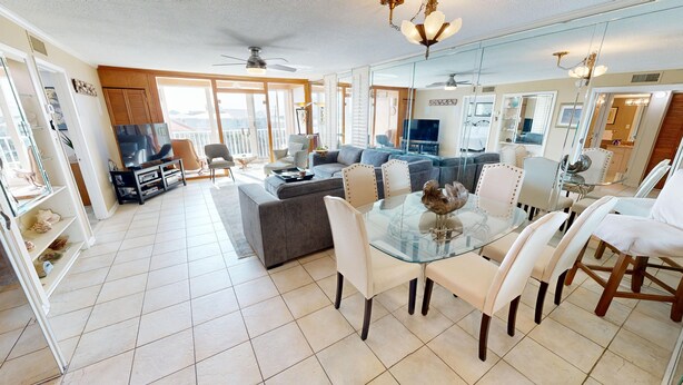 A spacious living area with a glass dining table, comfortable seating, a television, and a balcony with a view. - Dolphin Point 406b 2 Bedroom Condo (Destin)