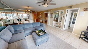 A spacious living room with a large sectional sofa, a coffee table, and a ceiling fan. There is a dining area with chairs and a table visible in the background. - Dolphin Point 406b 2 Bedroom Condo (Destin)