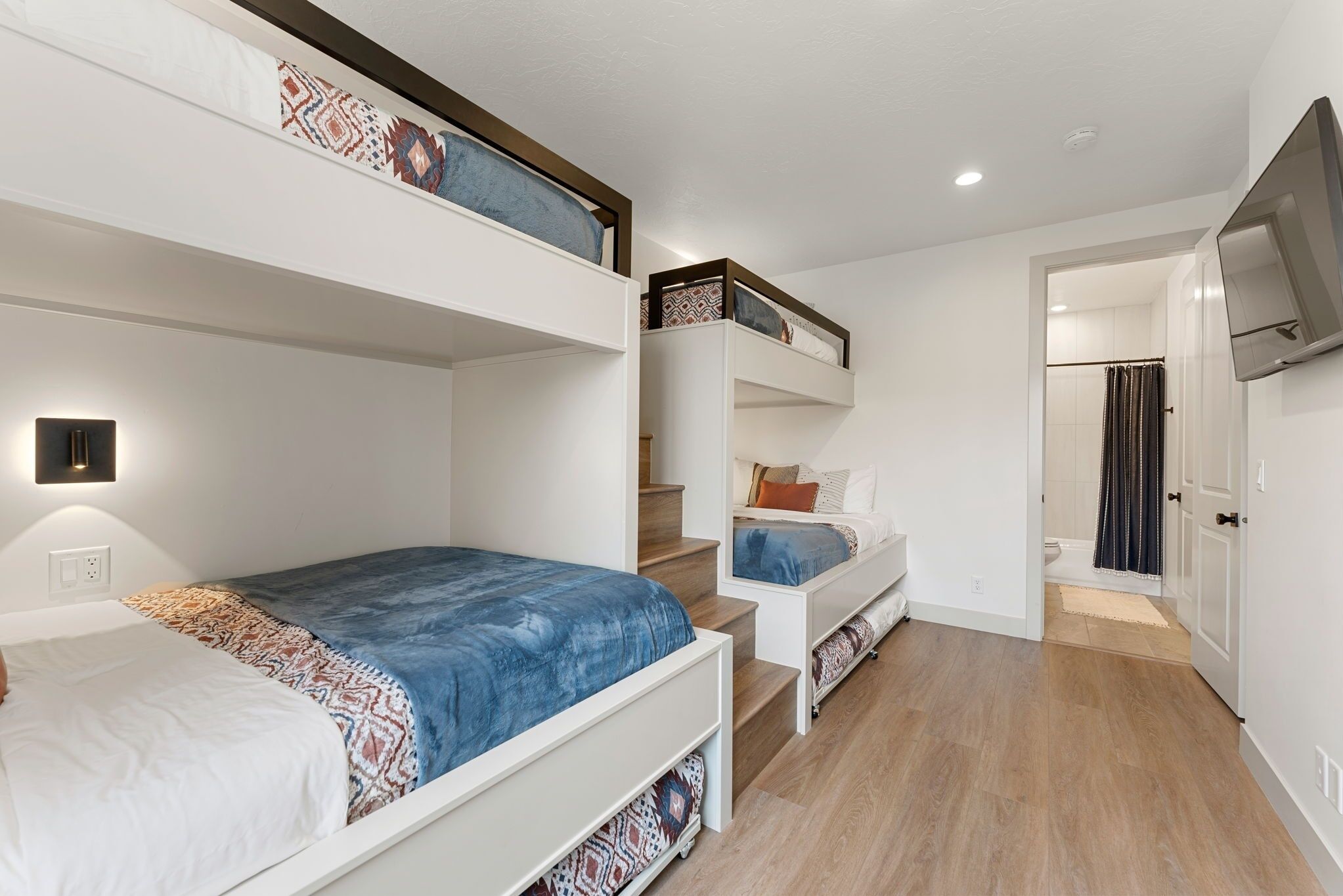 Une chambre à coucher de taille réduite, avec des lits superposés, un escalier, une télévision et une salle de bain équipée d’un rideau de douche.