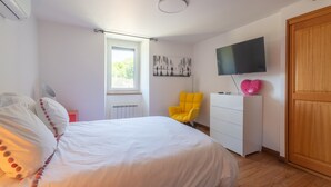 Een slaapkamer met een bed, een raam, een televisie, een stoel en een dressoir.
