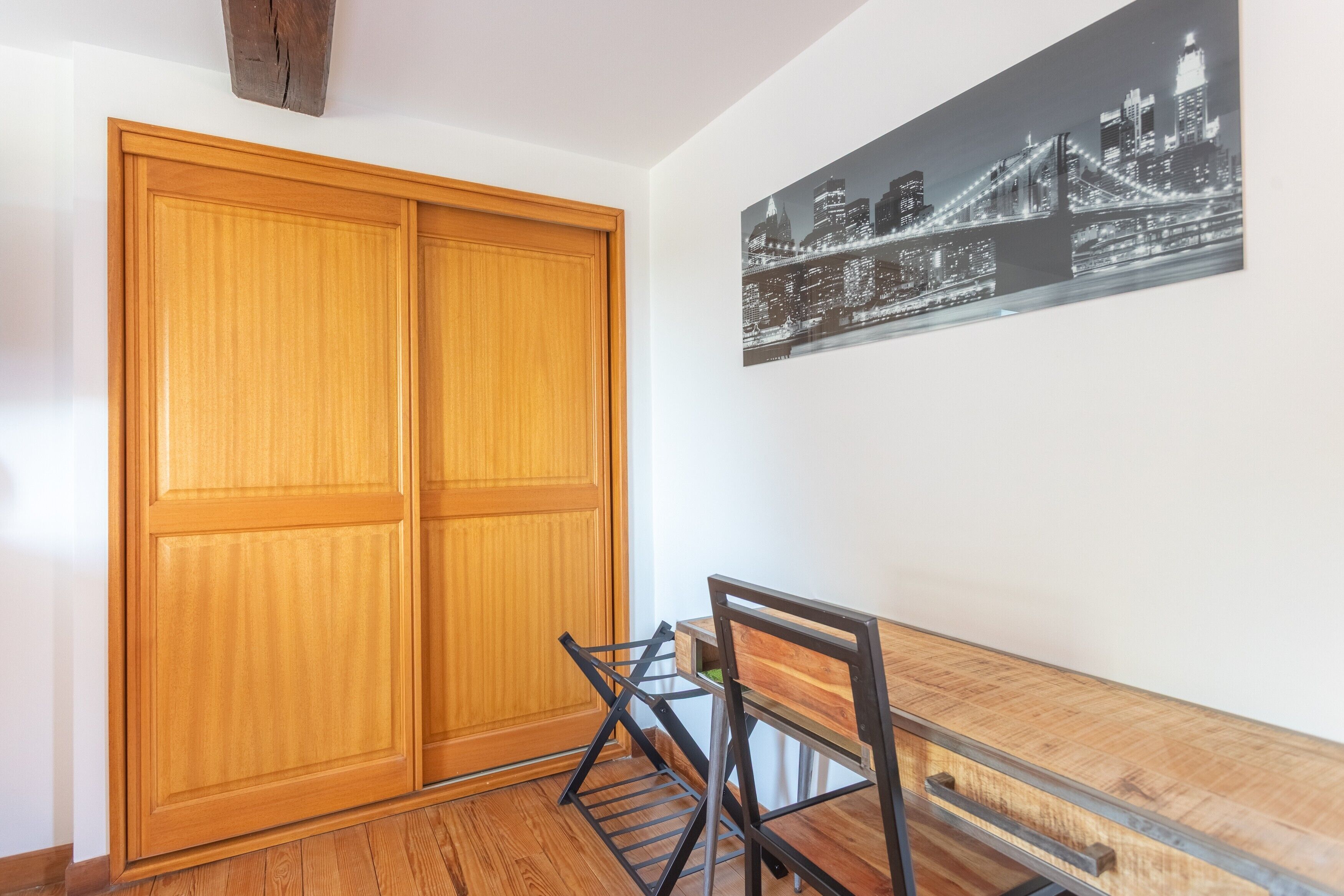 A room with a wooden wardrobe, a dining table with chairs, and a cityscape painting on the wall.