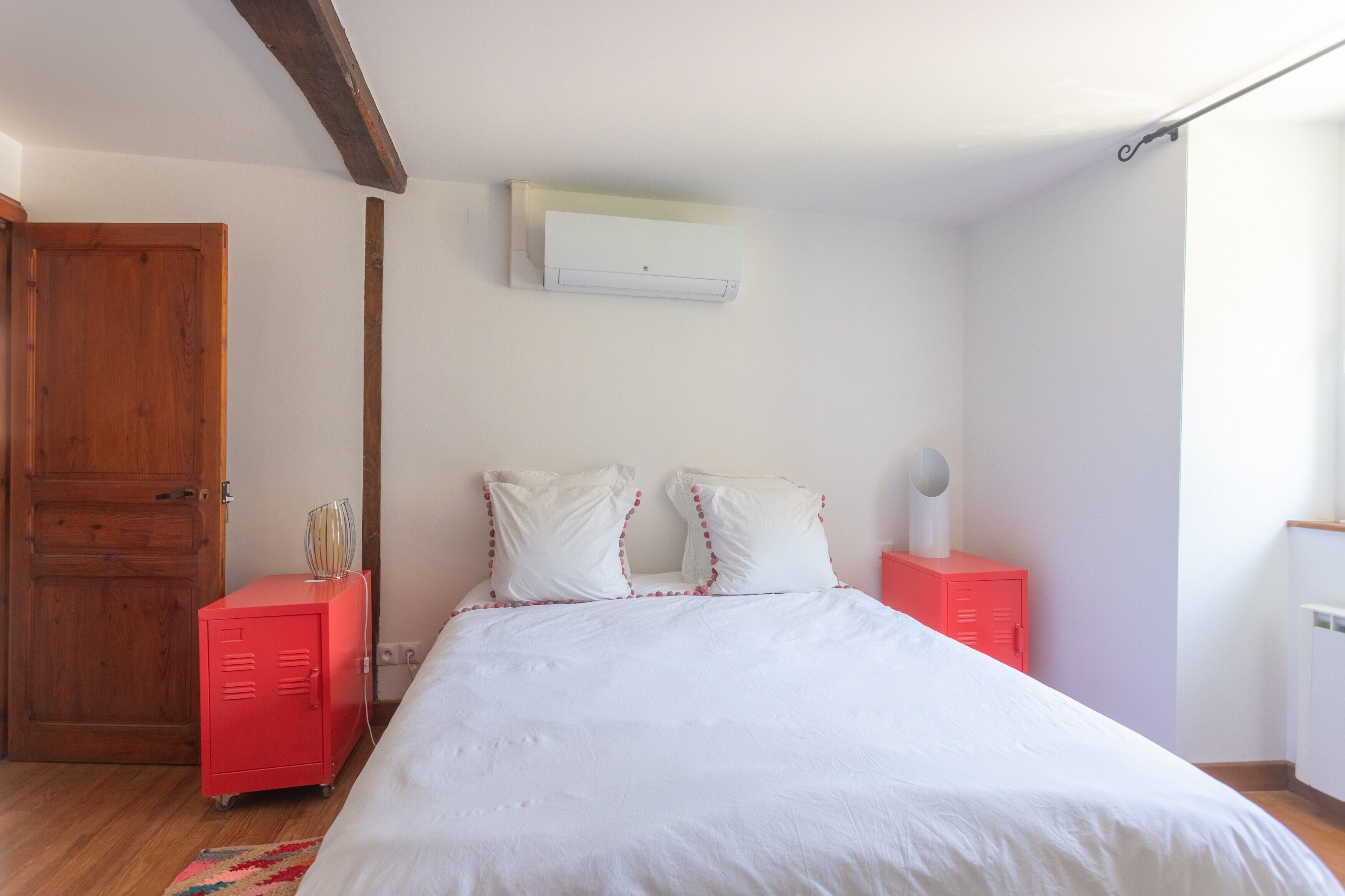 Un dormitorio con una cama, dos mesitas de noche, un armario rojo, una puerta de madera y un equipo de aire acondicionado.