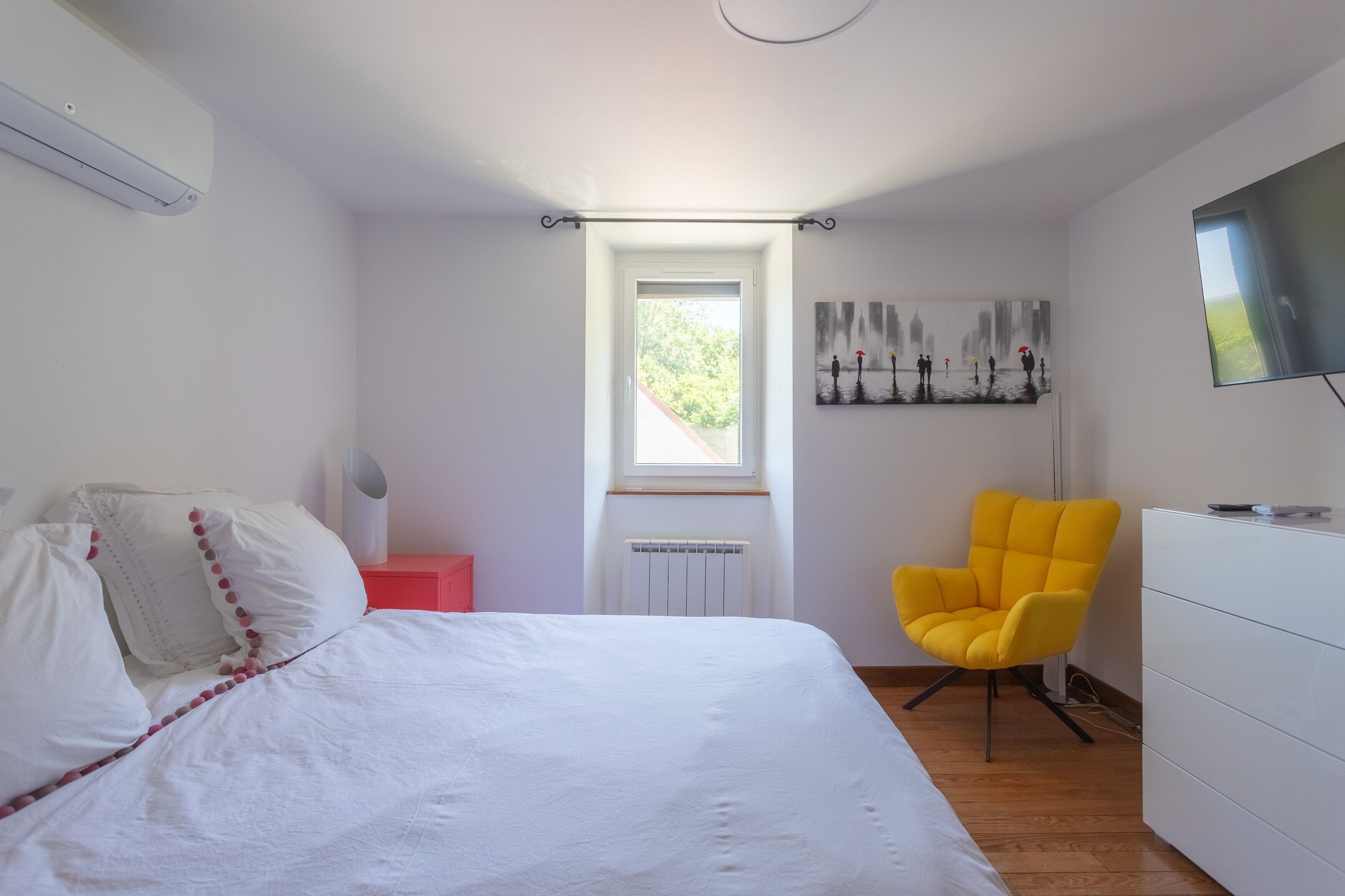 Ein Schlafzimmer mit einem Bett, einem Fenster, einer Heizung, einem Sessel und einem Fernseher.