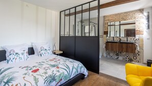 A bedroom with a bed, a yellow chair, a bathroom with a mirror, and a tiled backsplash. - Guest Room Domaine Cherps Spa & Pool – Serenity (Vielleségure)