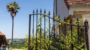 A wrought iron gate with climbing plants, a palm tree, and a building with a tiled roof. - Guest Room Domaine Cherps Spa & Pool – Serenity (Vielleségure)