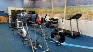 Et fitnesscenter med forskellig træningsudstyr, et blåt tæppe og et muralmaleri af en strandscene.