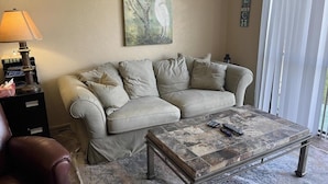 En stue med en beige sofa, et sofabord, en lampe og et billede på væggen.