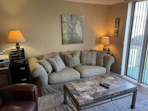 A living room with a beige sofa, a coffee table, and a lamp. - Vantage Pointe 138 - Condo Across The Street In Daytona Beach 1 Bedroom Condo (Daytona Beach)