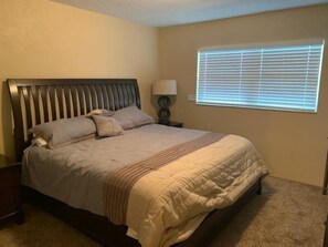A bedroom with a bed, a nightstand, a lamp, and a window with blinds. - Vantage Pointe #222 1 Bedroom Condo (Daytona Beach)