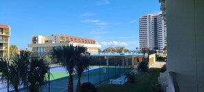 A tennis court with a net, surrounded by buildings, palm trees, and a clear sky. - Vantage Pointe #222 1 Bedroom Condo (Daytona Beach)