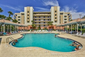 A swimming pool with lounge chairs and a building with multiple balconies in the background. - Kid Friendly Condo With Pool, Basketball, Bocce, Hot Tub, And More! 3 Bedroom Condo (New Smyrna Beach)