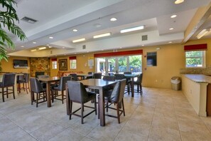 A spacious indoor dining area with multiple tables and chairs, a kitchen counter, and a large window providing natural light. - Kid Friendly Condo With Pool, Basketball, Bocce, Hot Tub, And More! 3 Bedroom Condo (New Smyrna Beach)