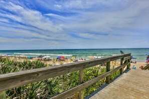 A wooden boardwalk leading to a beach with umbrellas and people. - Kid Friendly Condo With Pool, Basketball, Bocce, Hot Tub, And More! 3 Bedroom Condo (New Smyrna Beach)