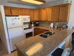 A kitchen with wooden cabinets, a granite countertop, a refrigerator, a microwave, a stove, and a sink. - Updated Condo Across The Street From Daytona Beach, Lots Of Amenities 1 Bedroom Condo (Daytona Beach)
