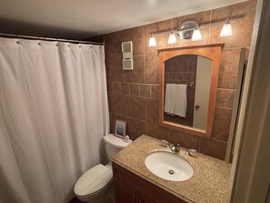 Casa de banho com cortina de chuveiro, sanita, lavatório com espelho em cima e toalha pendurada na parede.