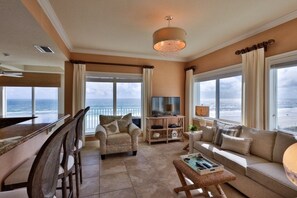 Ein geräumiges Wohnzimmer mit großem Fenster zum Meer, einem bequemen Sofa, einem Fernseher und einem Essbereich mit Stühlen.