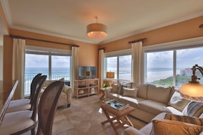 A spacious living room with a large window offering a view of the ocean, a television, and a comfortable seating area. - Oceanfront Condo With Beautiful Views 2 Bedroom Condo (New Smyrna Beach)