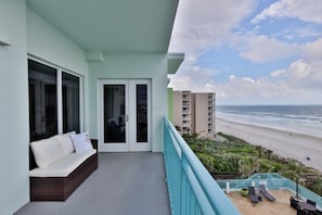 A balcony with a view of the beach, a sofa, and a dining area with chairs. - Oceanfront Condo With Beautiful Views 2 Bedroom Condo (New Smyrna Beach)