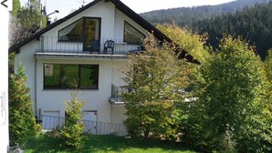 A two-story house with a balcony, surrounded by greenery and hills in the background. - FeWo Wald Idyllika (Willingen)