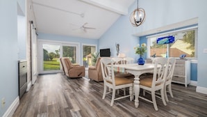 A spacious dining area with a high ceiling, a ceiling fan, and a large window offering a view of the outdoors. - Beautifully Decorated Townhome In Sugar Mill Nsb 2 Bedroom Townhouse (New Smyrna Beach)