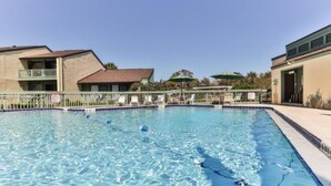 A swimming pool with clear water, surrounded by a fence and a building with a balcony. - Beautifully Decorated Townhome In Sugar Mill Nsb 2 Bedroom Townhouse (New Smyrna Beach)