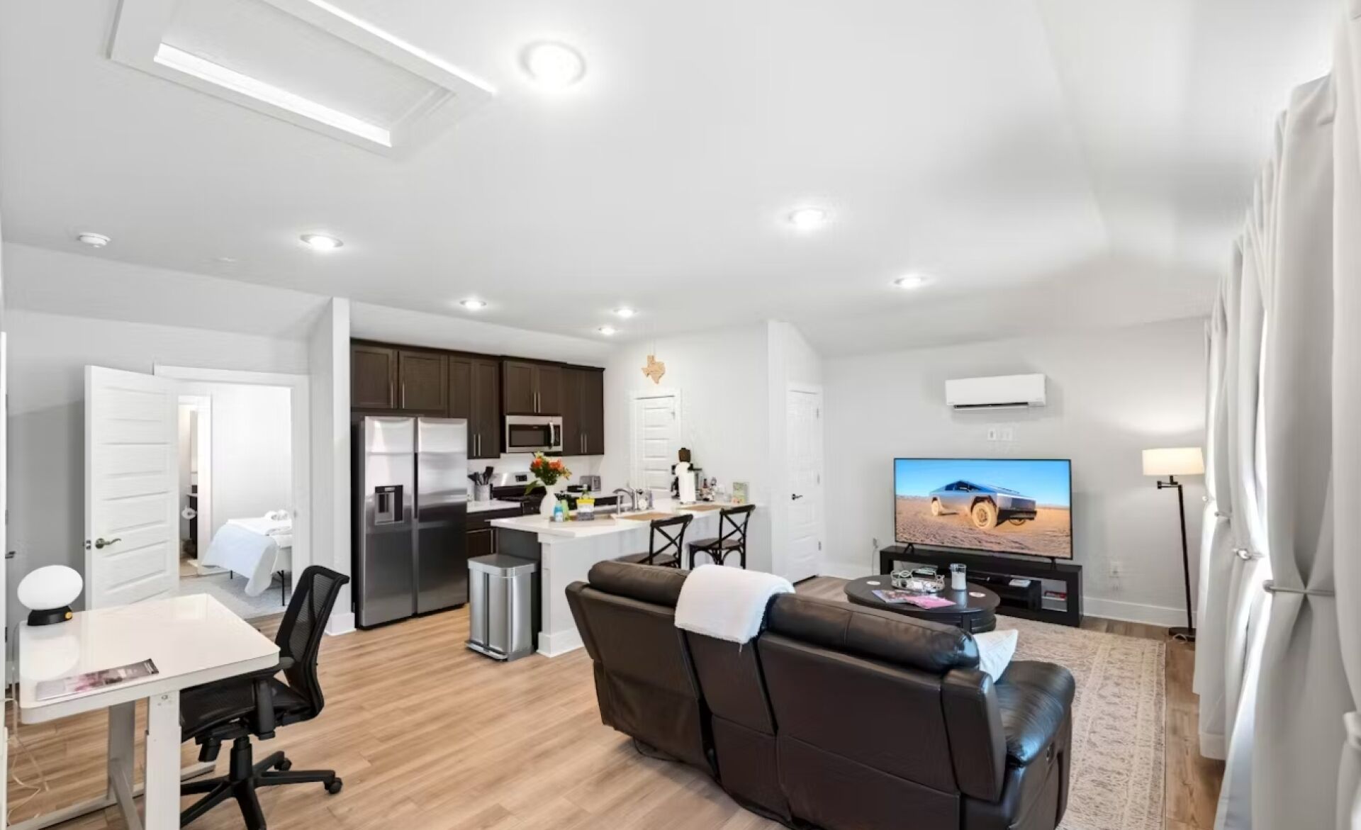 A modern living space with a kitchen, dining area, and a seating area with a sofa and TV.