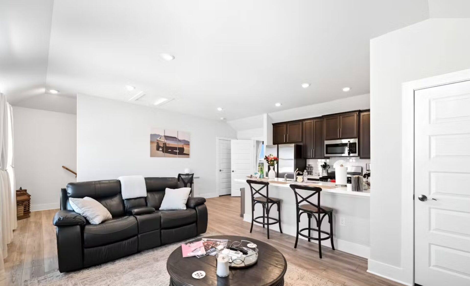 A modern living room with a black leather sofa, a coffee table, and a kitchen area with dark cabinets and a microwave.