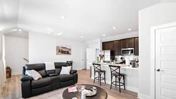 A modern living room with a black leather sofa, a coffee table, and a kitchen area with dark cabinets and a microwave.