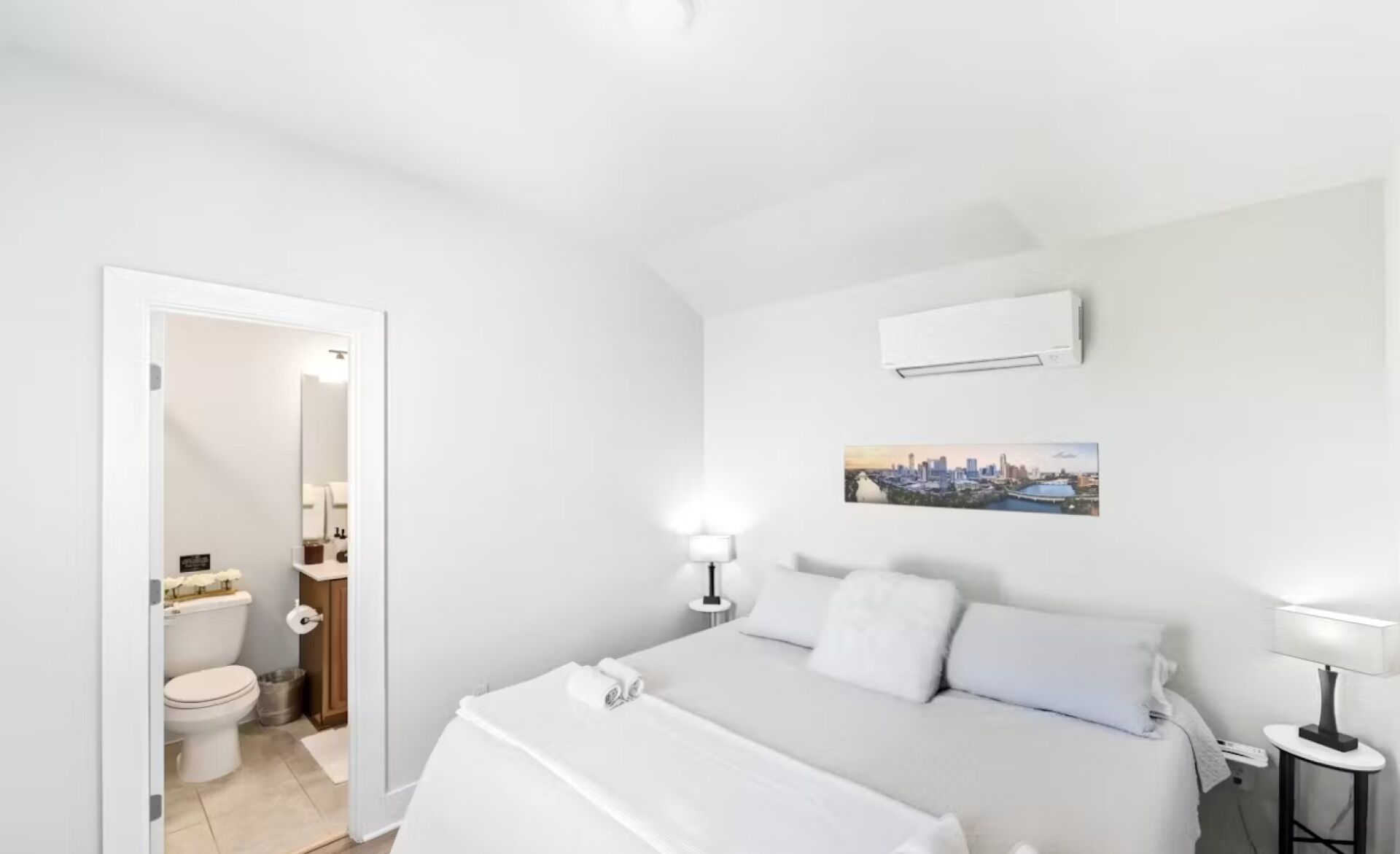 A hotel room with a bed, a bathroom, and a cityscape painting on the wall.