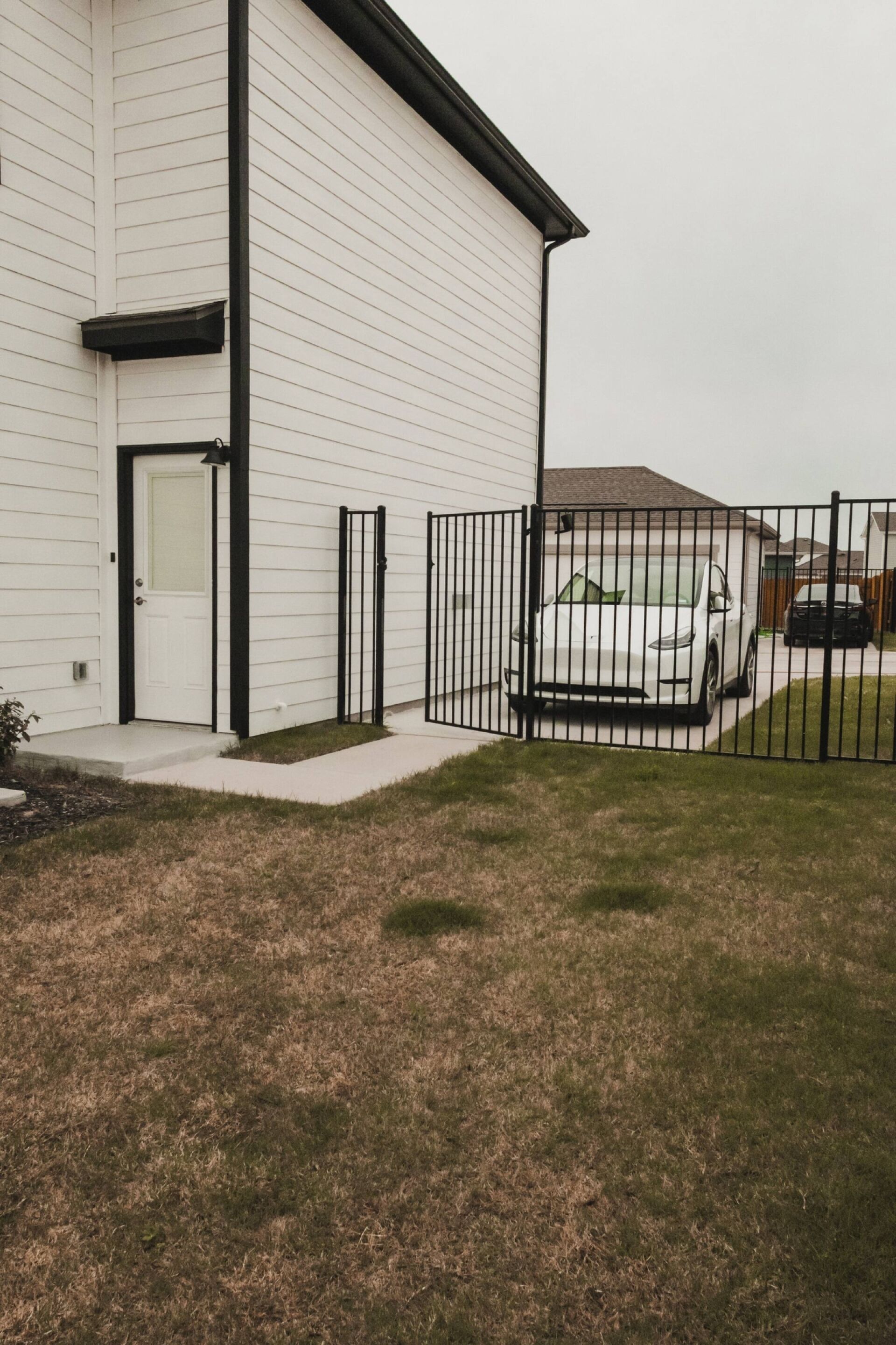 A white building with a black door, a gated driveway, and a parked white car.