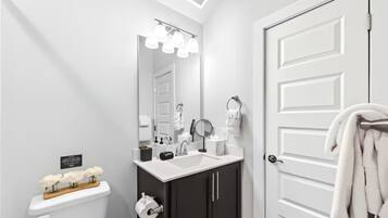 A modern bathroom with a white sink, dark cabinets, a large mirror, and a white door.