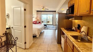 Una habitación de hotel con cama, un balcón con vistas, kitchenette y ventilador de techo.
