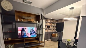 Moderni olohuone, jossa on sohva, sohvapöytä, televisio ja kirjahylly.