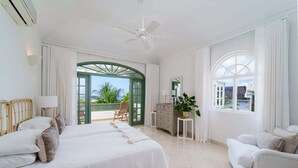 A spacious bedroom with a large bed, a sitting area with a chair, and a view of the outdoors. - Sugar Hill - Jade Vine 3 Bedroom Villa (Holetown)