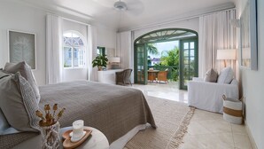 A spacious bedroom with a large bed, a sitting area with a sofa, and a view of the outdoors. - Sugar Hill - Jade Vine 3 Bedroom Villa (Holetown)